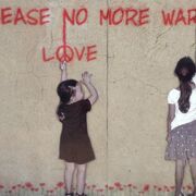 zwei Kinder vor brauner Hauswand mit rotem Graffiti-Schriftzug "Please no more war. Love"